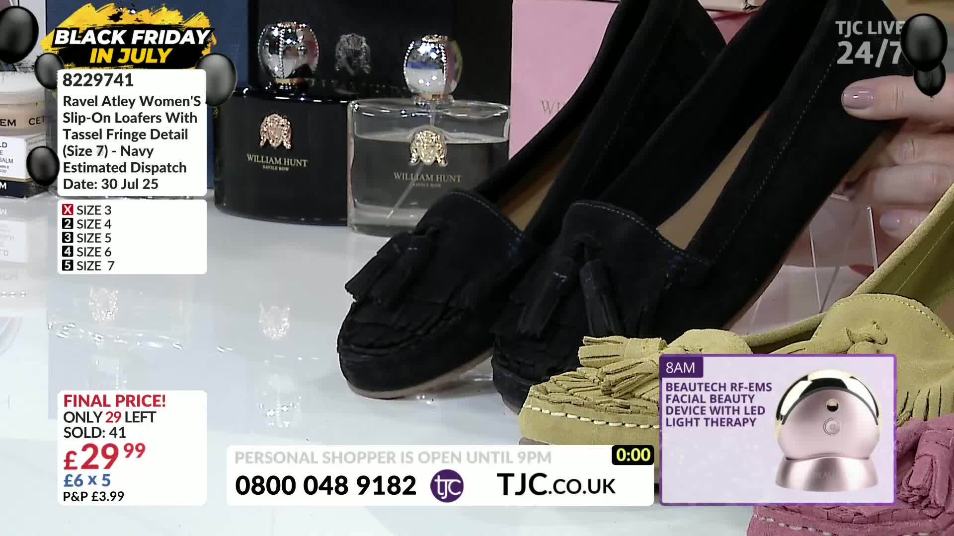 A pair of navy slip-on loafers with tassels is being held up, showcasing the details. The TJC studio features other shoes and beauty products, with a "Black Friday in July" deal displayed on screen.
