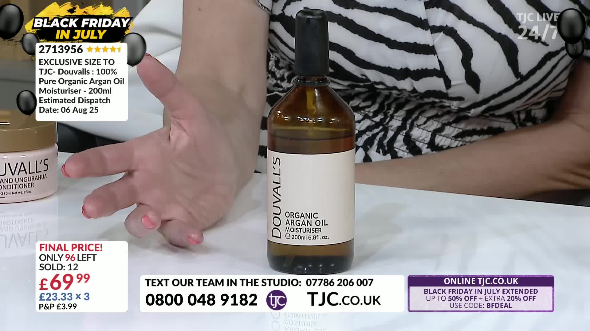 A woman's hand gestures towards a bottle of Douvall's Organic Argan Oil Moisturiser, positioned center-frame. The TJC studio backdrop features promotional text, including a Black Friday in July sale.
