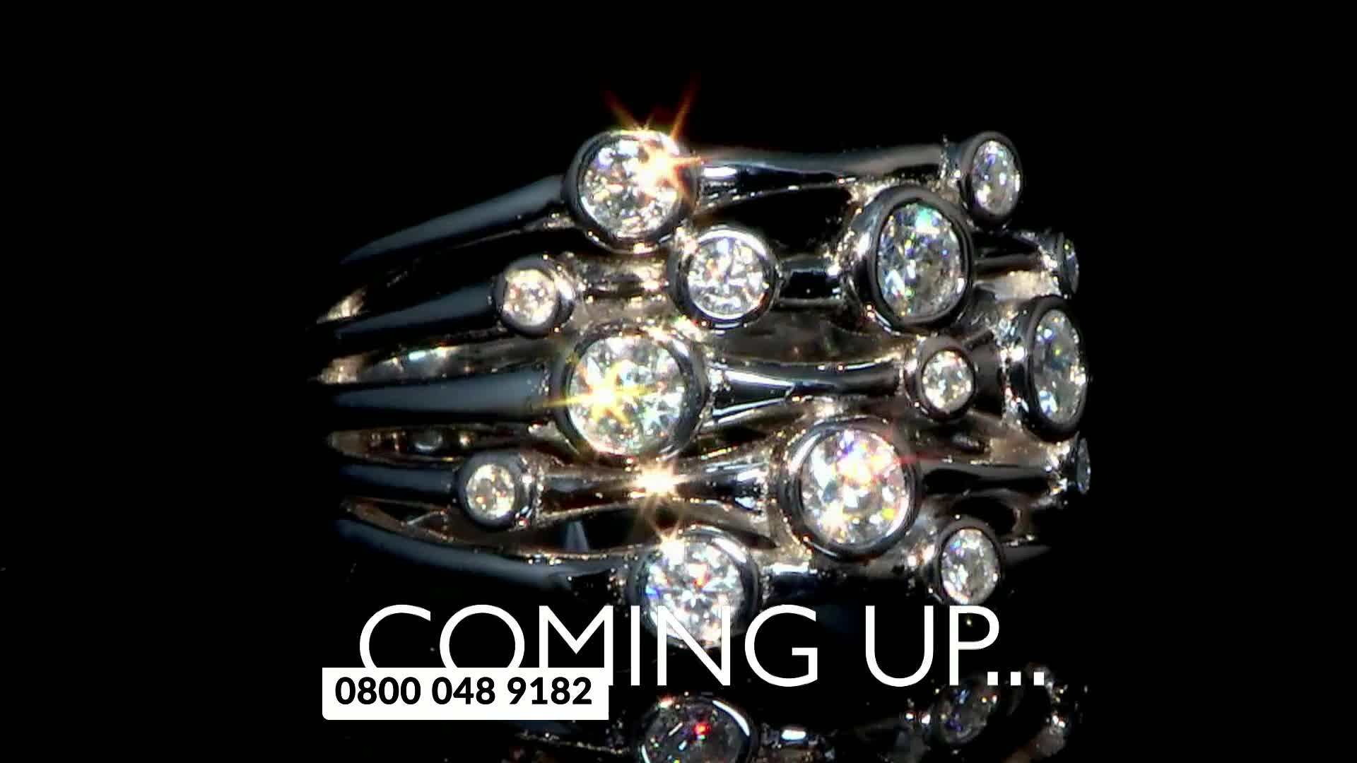 A multi-layered ring, studded with sparkling stones, is the focus. The words "COMING UP..." and a phone number appear below it, likely a preview on a UK shopping channel.
