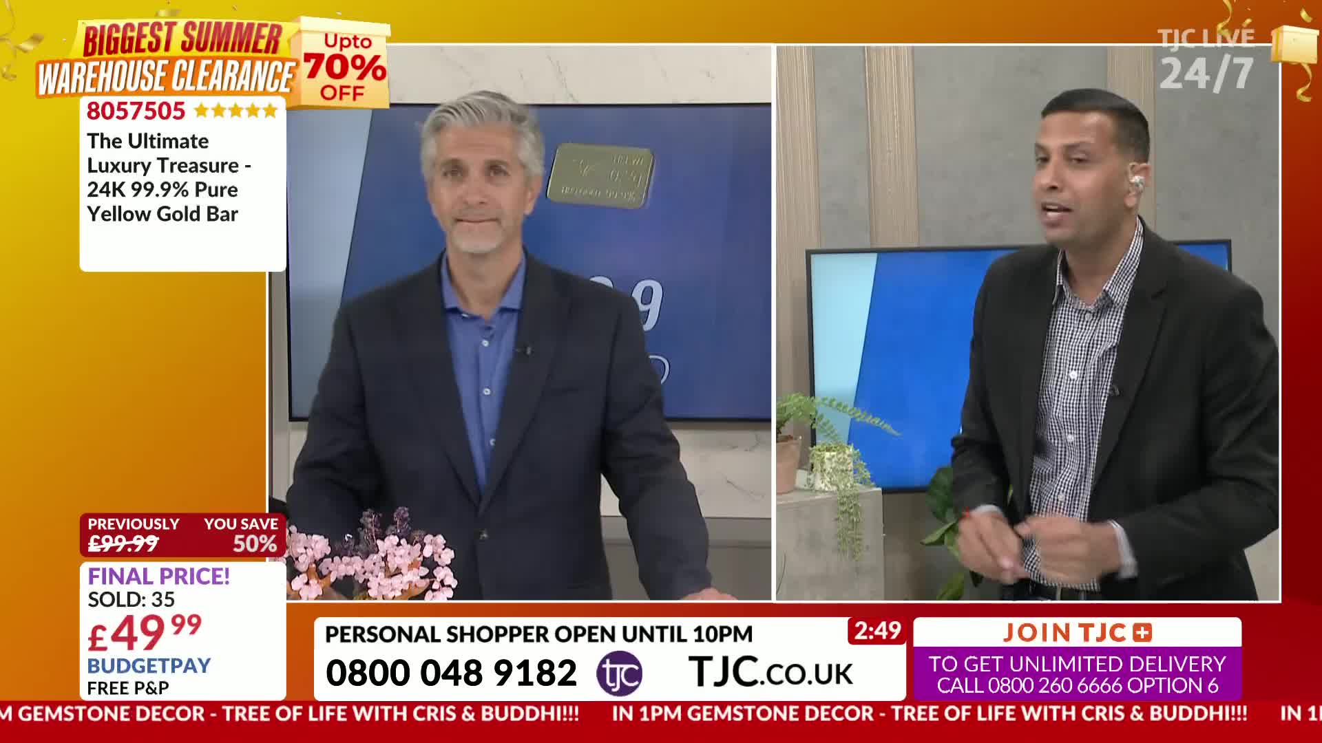 Two men in suits are on a TJC set, one gesturing with his hands as he speaks. The screen behind them advertises a gold bar at a reduced price.
