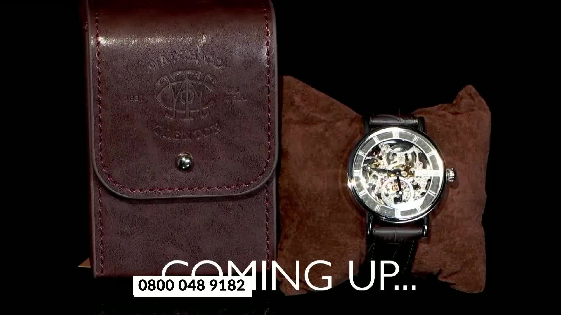 A skeleton watch with a black leather strap rests on a brown cushion next to a leather watch case. "Coming Up..." is written in white text below.
