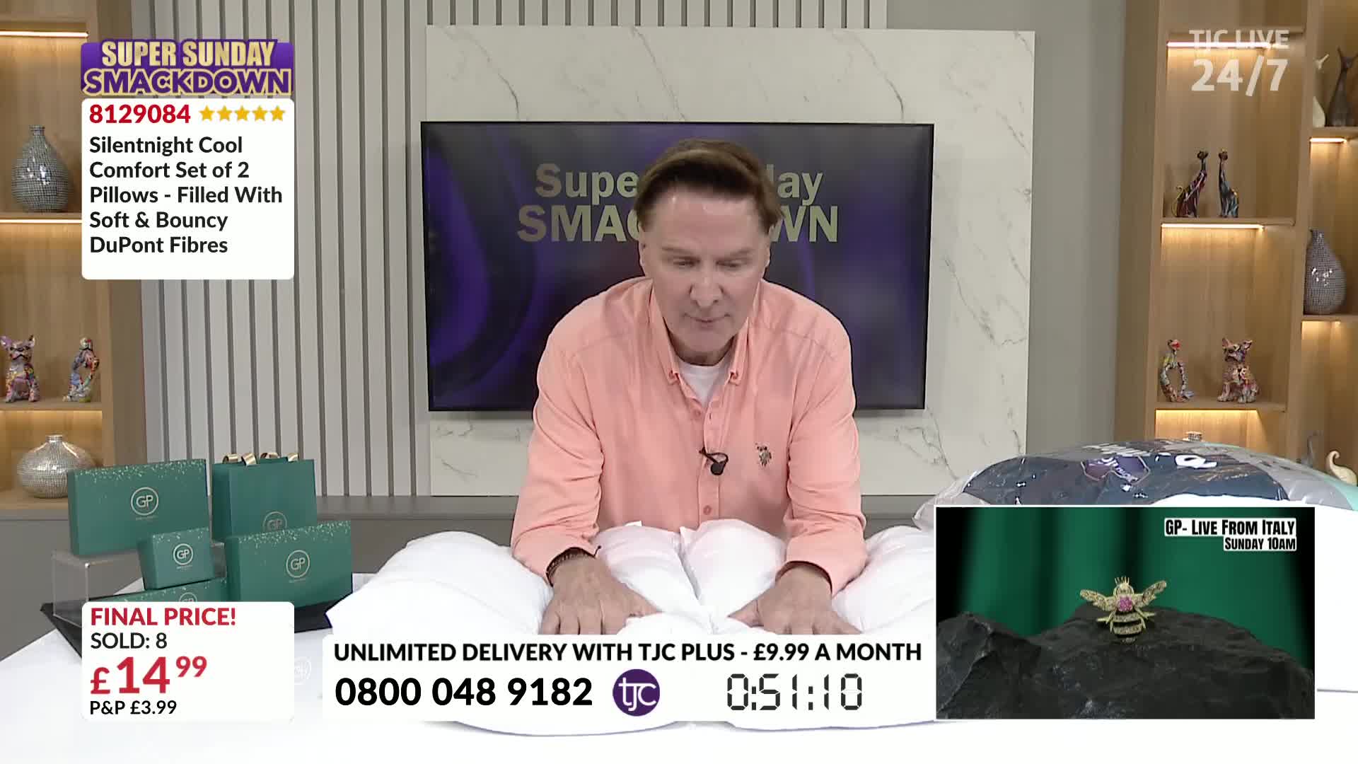 A man in a pink shirt sits amongst fluffy white pillows, demonstrating their softness. He's on a live shopping show, offering a set of pillows for sale on TJC.
