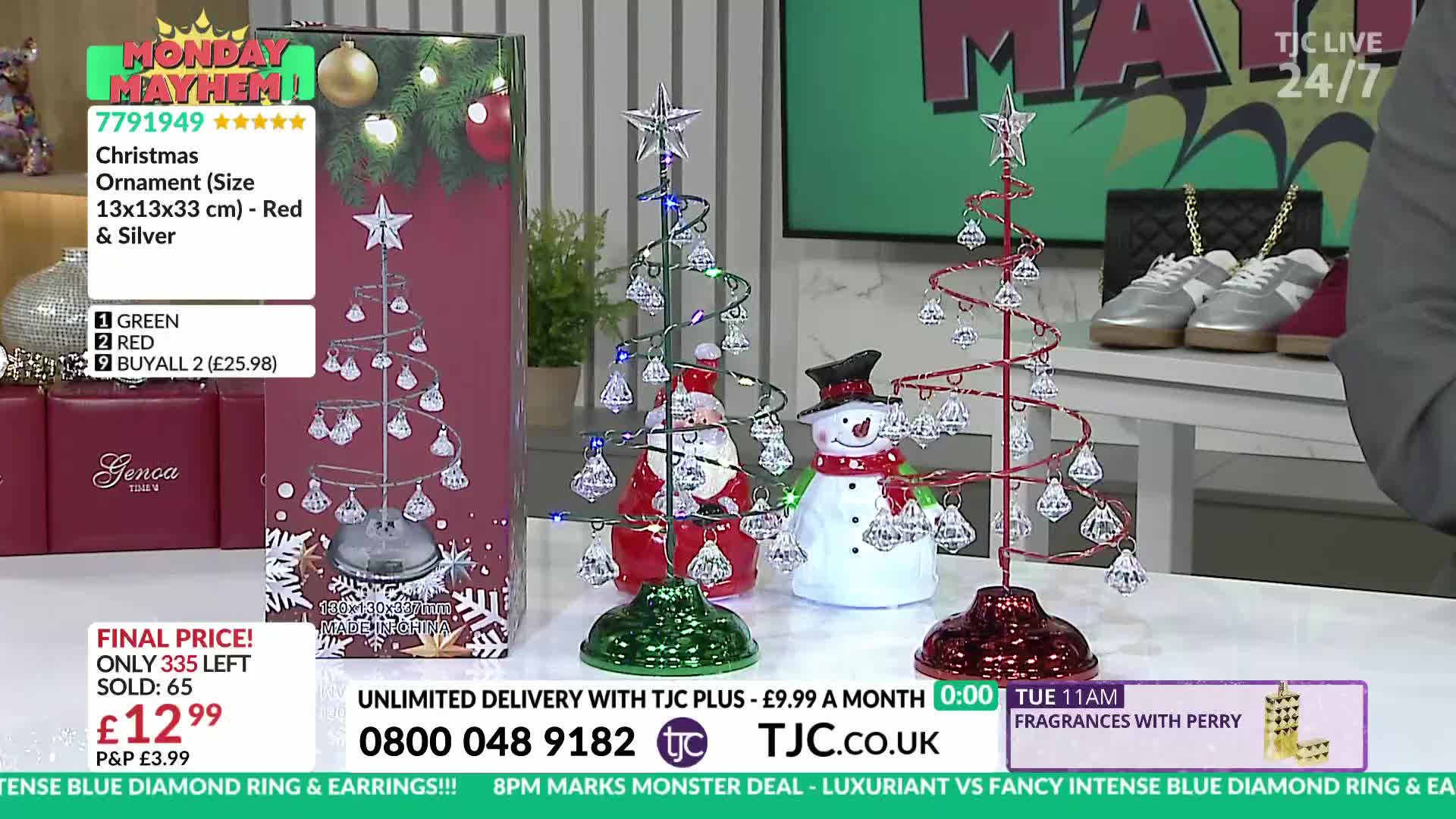 Three decorative Christmas trees, each with a spiral wire frame and dangling crystal ornaments, are on display. A box showing a similar ornament sits to the left, and a screen in the background displays the TJC logo and the current price.
