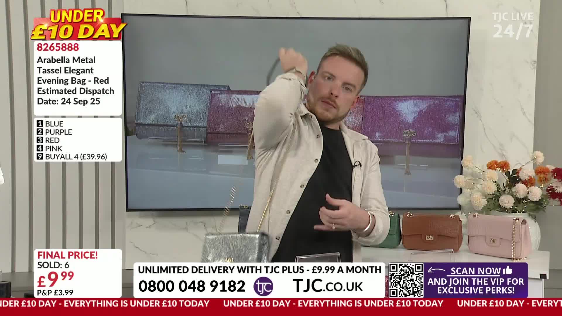 A man in a light jacket holds a silver evening bag, demonstrating its chain strap. He's on a TJC set, showing off the bag's features to the camera.

