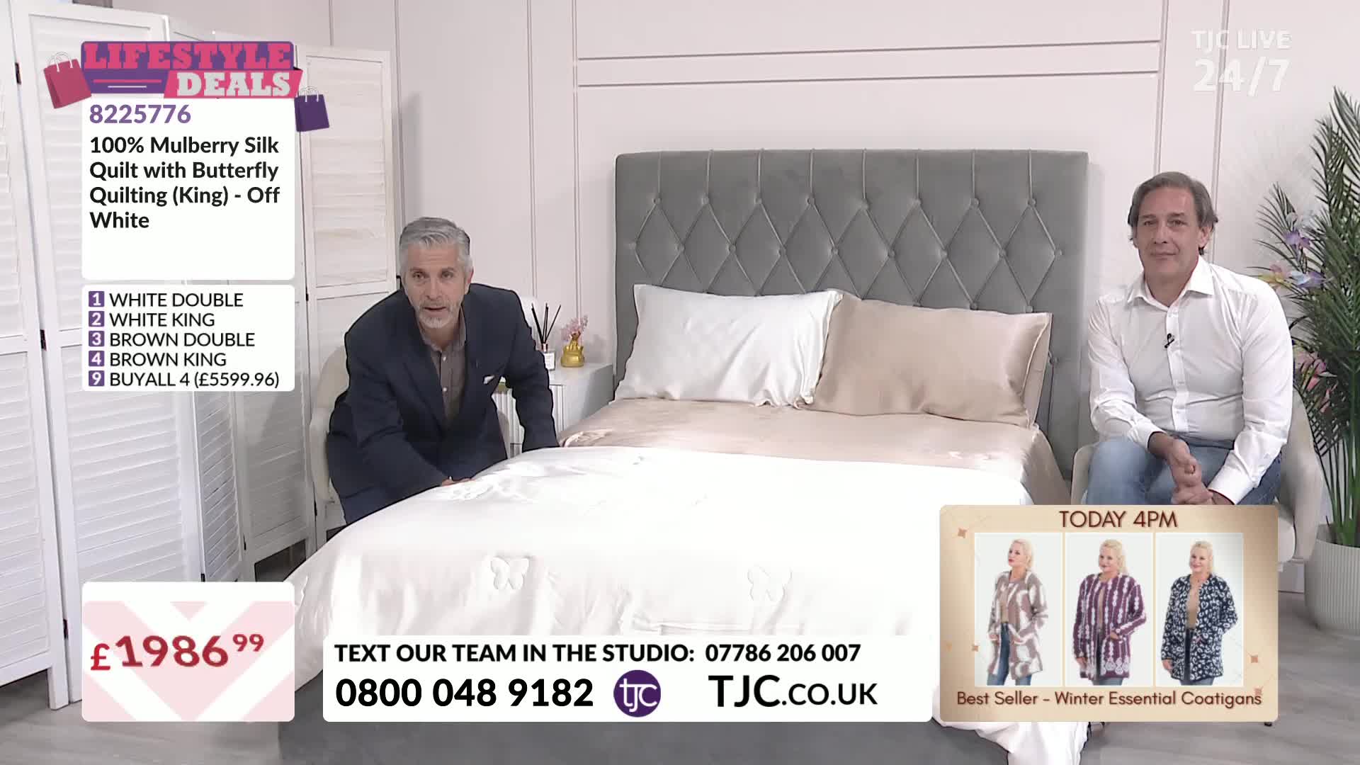 A man in a suit is smoothing a large, white quilt on a bed, while another man sits nearby. The TJC studio is set up with a bed and a display of products for sale.
