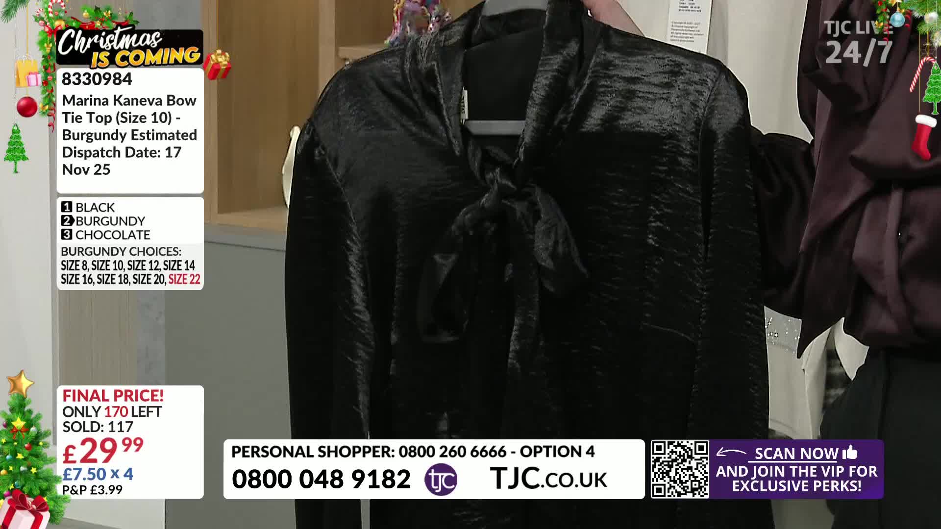 A dark, shiny top with a bow is held up for display. The TJC logo and a "Christmas is Coming" banner are visible in the corner.
A dark, shiny top with a bow is held up for display. The TJC logo and a "Christmas is Coming" banner are visible in the corner.