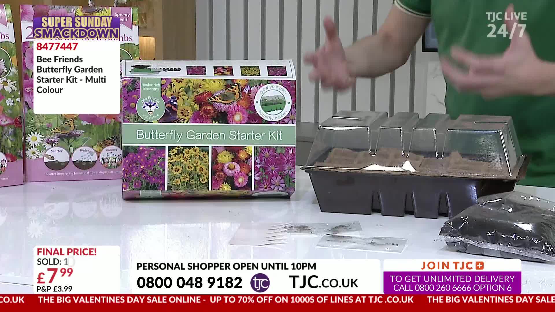 A presenter on TJC Live gestures enthusiastically over a butterfly garden starter kit and a seed tray. The kit displays vibrant images of flowers and butterflies, promising a colourful bloom.