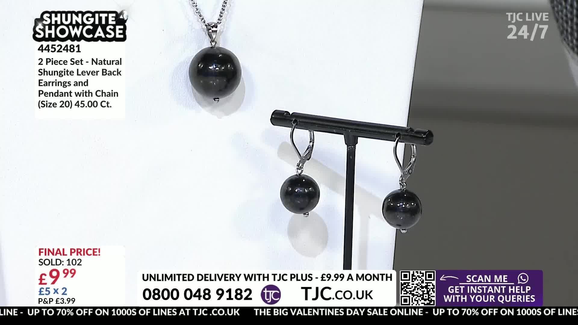 A pendant with a dark, smooth sphere hangs from a delicate silver chain. Nearby, a pair of matching earrings dangle from a black display stand.