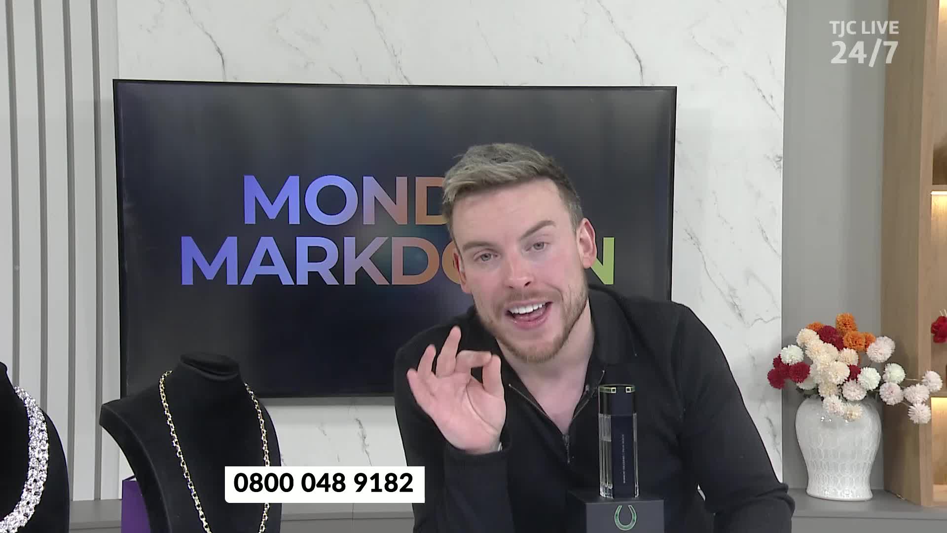 A man on TJC Live gestures with his right hand, forming a circle with his thumb and index finger. Behind him, a screen displays "MONEY MARKDOWN," and a phone number is visible at the bottom.