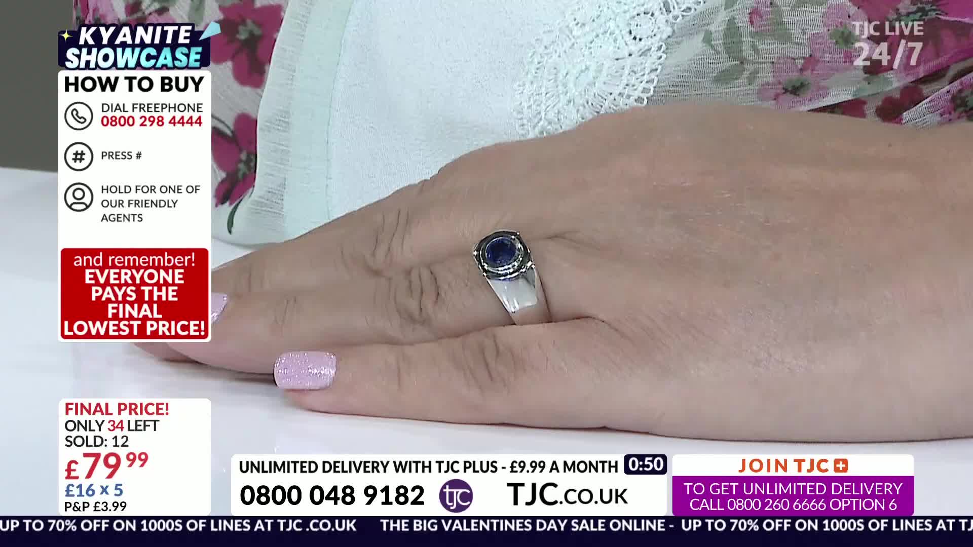 A hand displays a silver ring with a dark blue stone, its fingers adorned with pale pink nail polish. Text on the screen announces a Kyanite Showcase and provides ordering information for TJC.