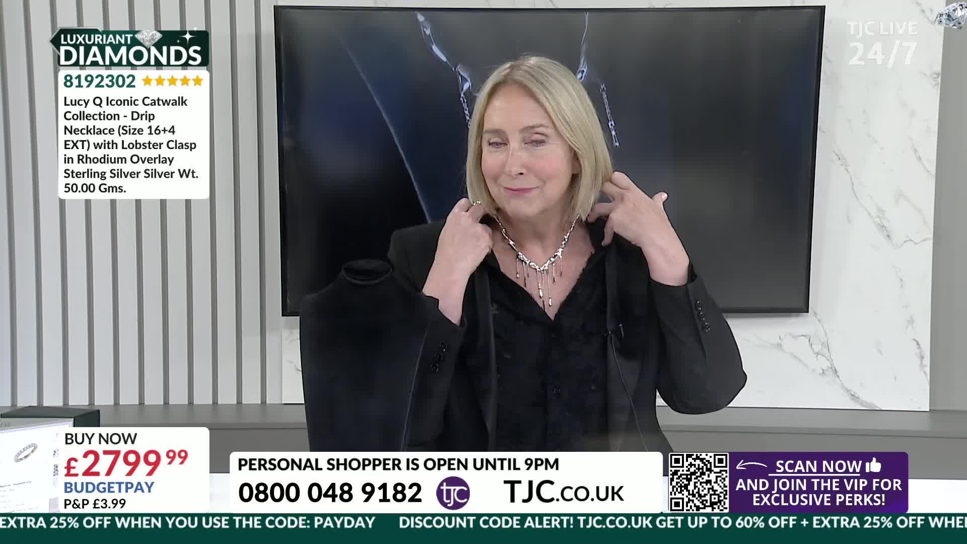 A woman adjusts a delicate silver necklace, its pendant drops swaying gently. On the screen behind her, a TJC logo flashes with the time.