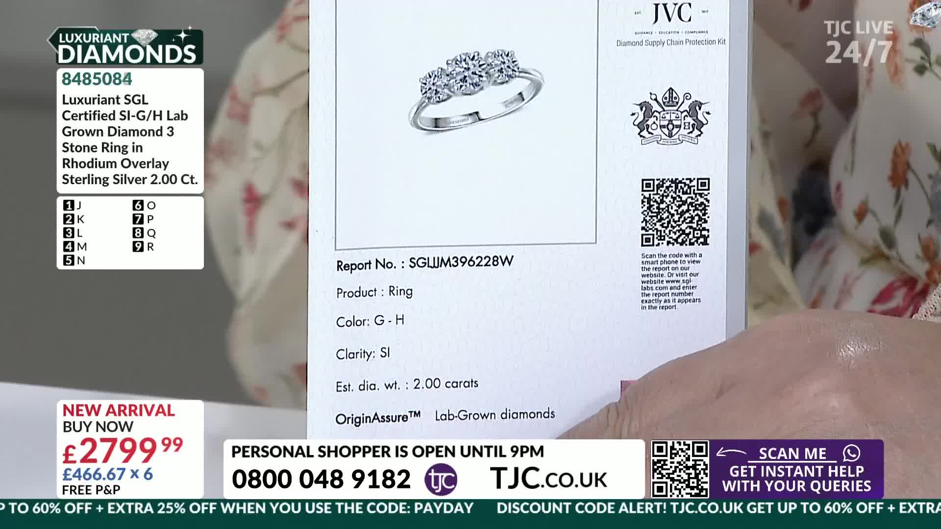 A hand holds up a certificate displaying a three-stone ring. The ring is set in rhodium-plated sterling silver with three prominent diamonds.