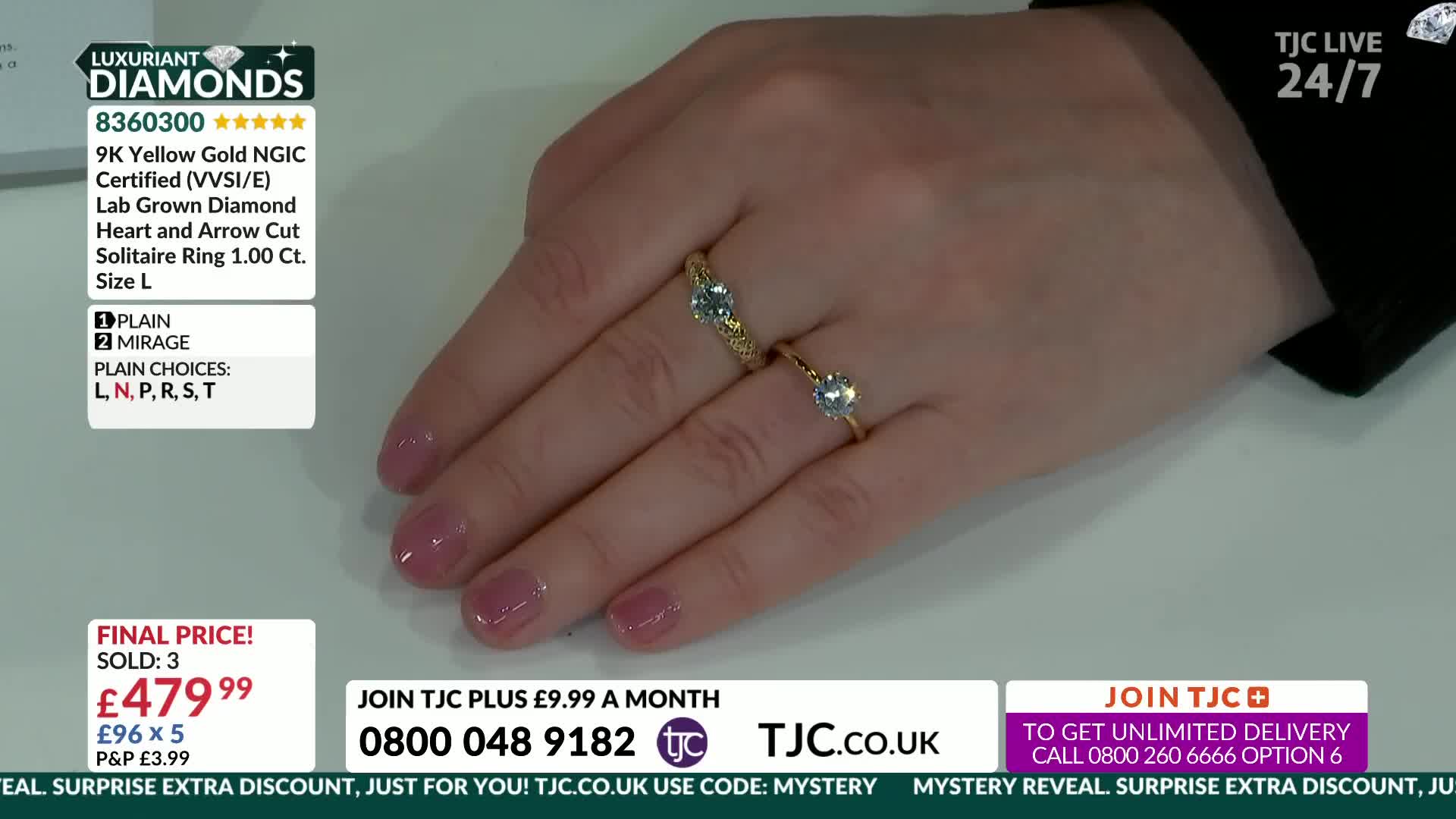 A hand displays two gold rings, one with a detailed band and a central stone, the other a simpler solitaire. The nails are painted a sheer pink.