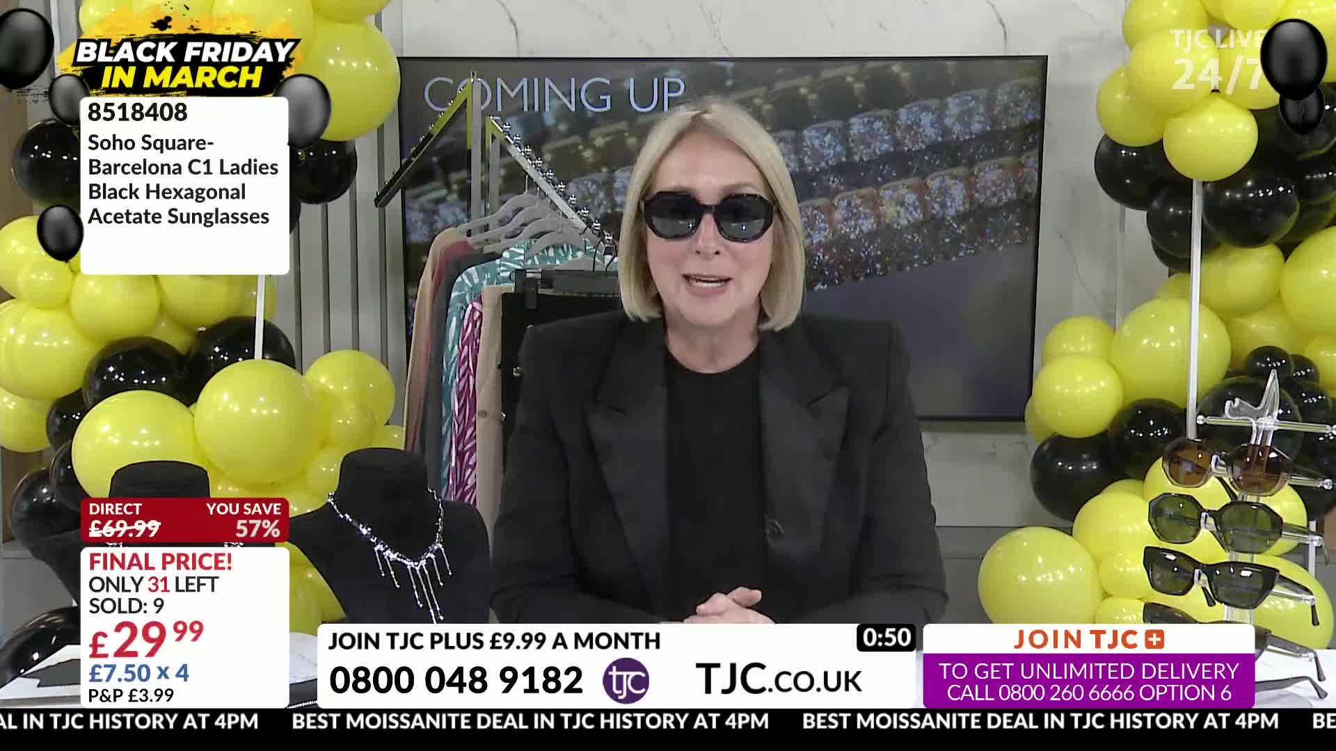 A woman in a black blazer and sunglasses stands before a display of sunglasses and jewelry. Yellow and black balloons create a festive backdrop for the TJC presentation.