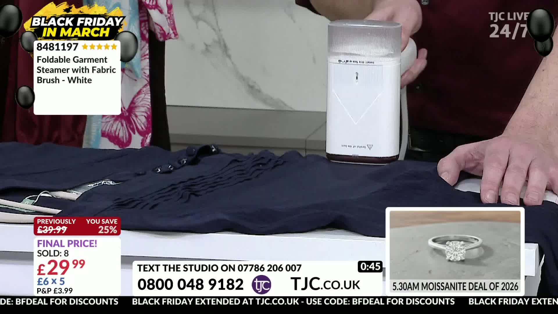 A white garment steamer glides over a dark blue shirt laid flat. A hand guides the steamer, smoothing out the fabric.