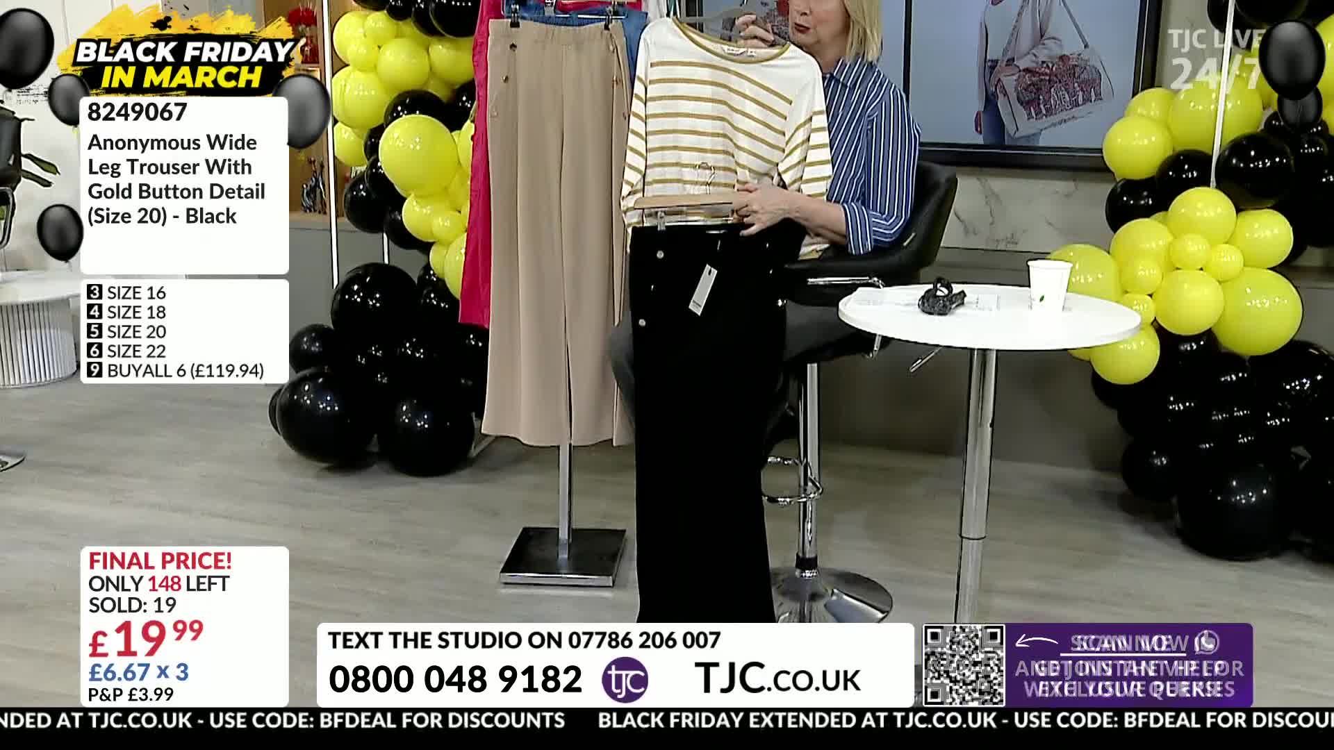 A woman in a striped shirt holds up a pair of black trousers with gold buttons. The TJC logo is visible, and the background is decorated with black and yellow balloons.