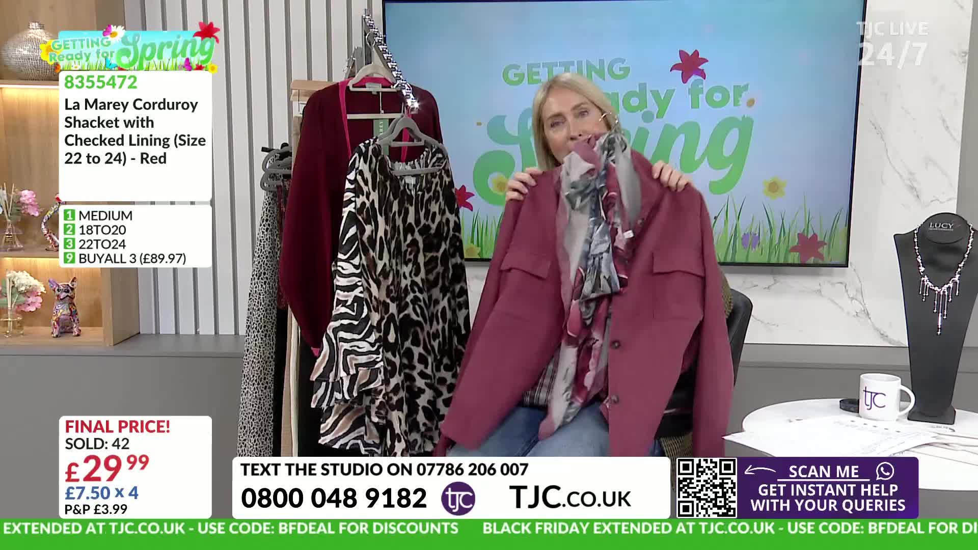A woman holds up a burgundy jacket with a floral scarf draped inside. To her left, a leopard-print top hangs on a hanger.