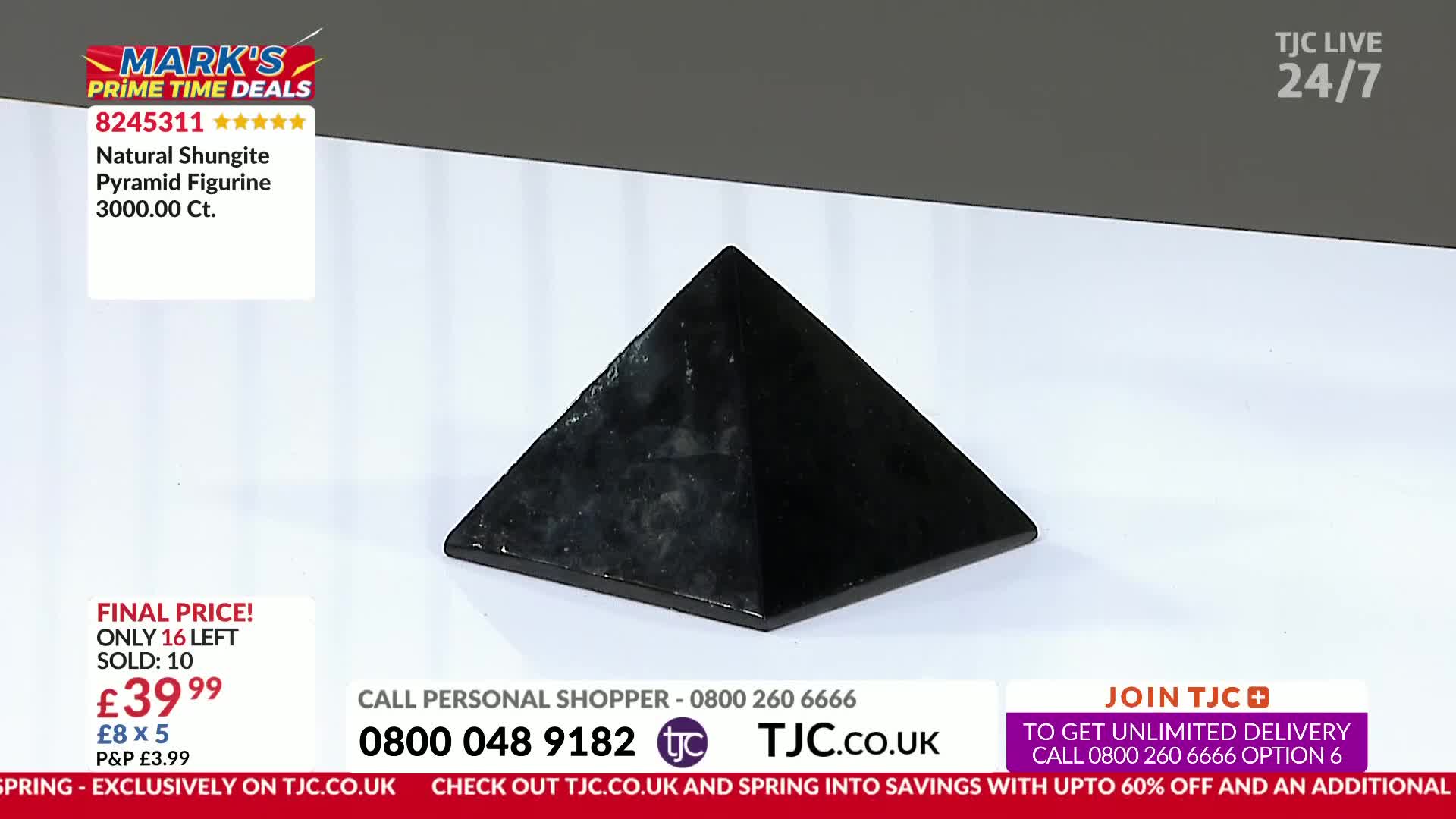 A dark, faceted pyramid sits on a white surface. Text overlays indicate it's a "Natural Shungite Pyramid Figurine" on sale for £39.99 through TJC.