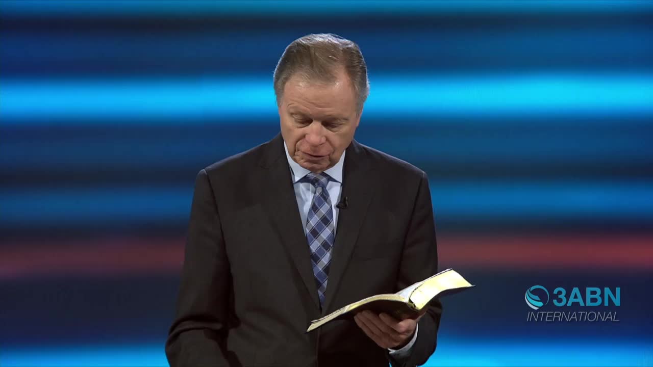 A man in a suit, tie askew, reads from a book with yellowed pages. The 3ABN International logo is visible in the corner against a backdrop of blue and red horizontal stripes.
