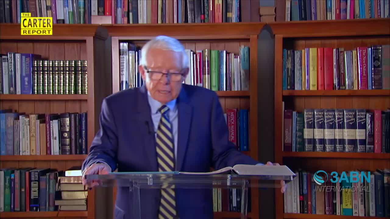 A man in a blue suit stands behind a clear podium, speaking into a microphone. He's surrounded by bookshelves, with the 3ABN International logo visible in the corner.
