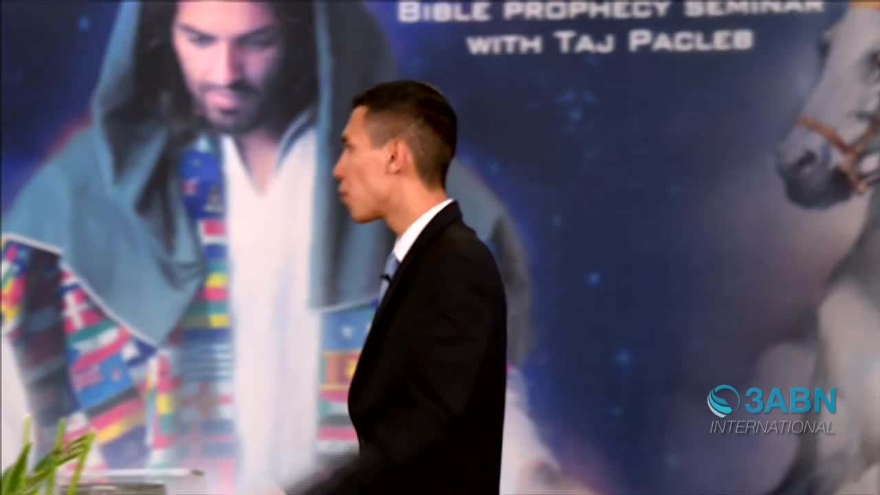 A man in a dark suit walks past a backdrop advertising a Bible prophecy seminar. Behind him, a logo for 3ABN International is visible.
