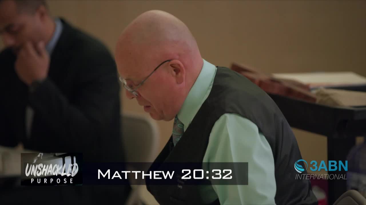 A man in glasses and a vest is looking down, his head slightly bowed. The 3ABN International logo is visible, and the words "Unshackled Purpose" and "Matthew 20:32" are displayed on the screen.
