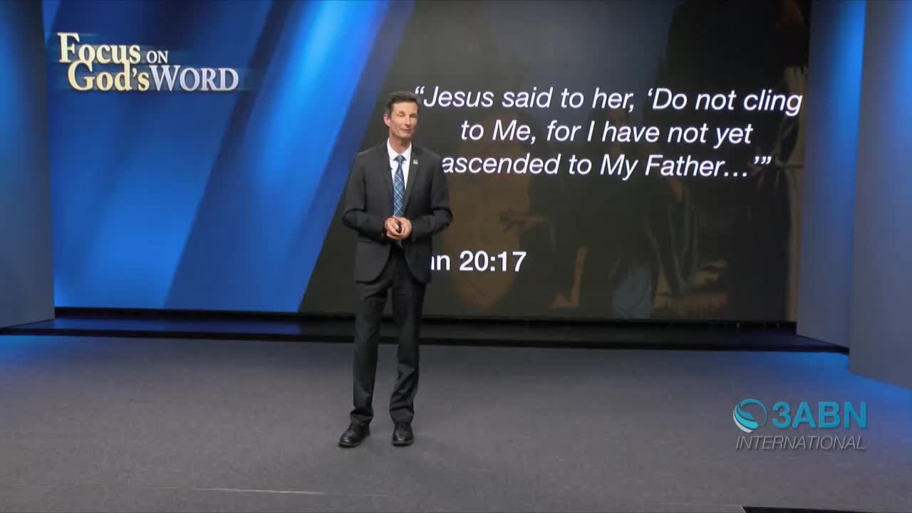 A man in a suit stands center stage, speaking in front of a screen displaying a Bible verse. The logo for 3ABN International is visible in the bottom right corner.
