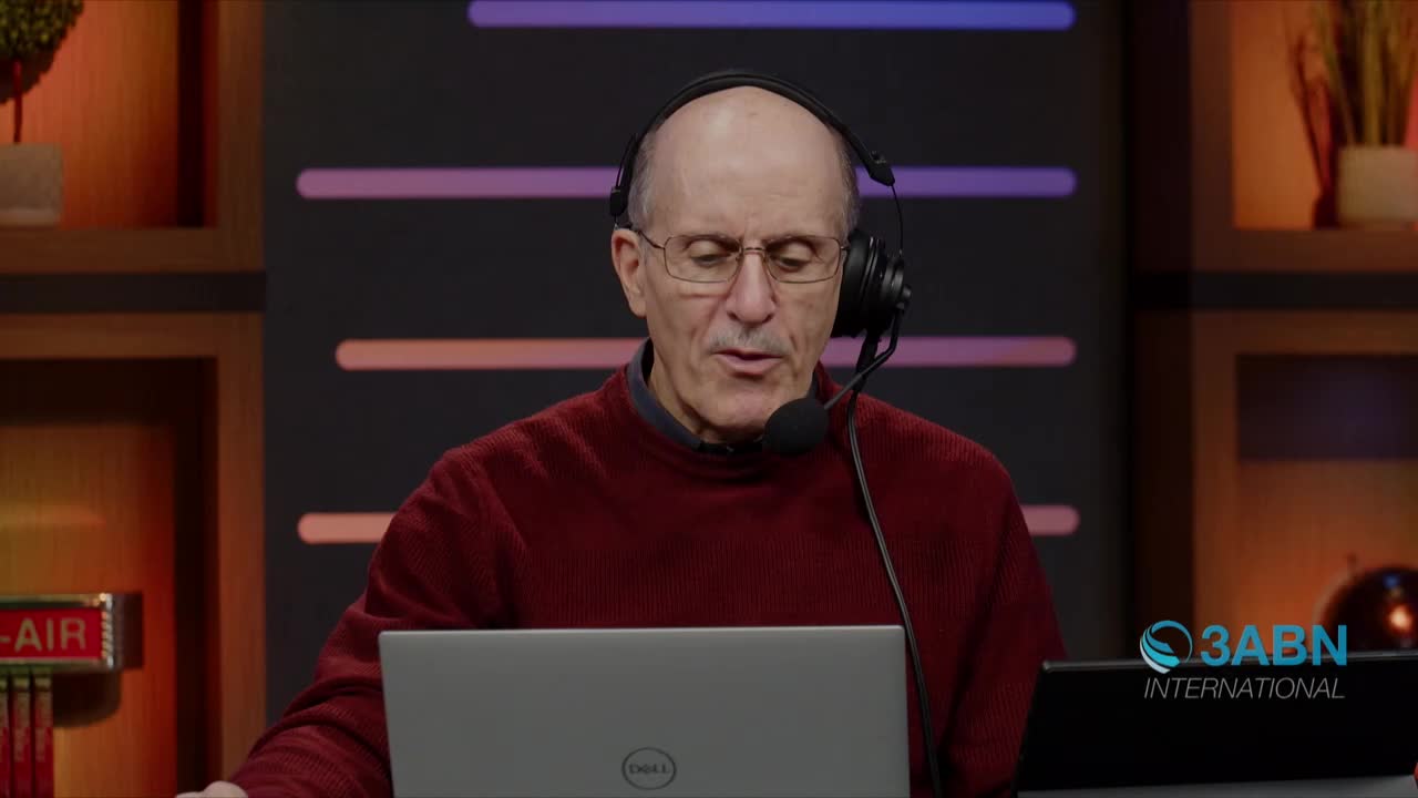 A man in a burgundy sweater and glasses speaks into a microphone, his eyes focused on a laptop. The 3ABN International logo is visible in the corner.
