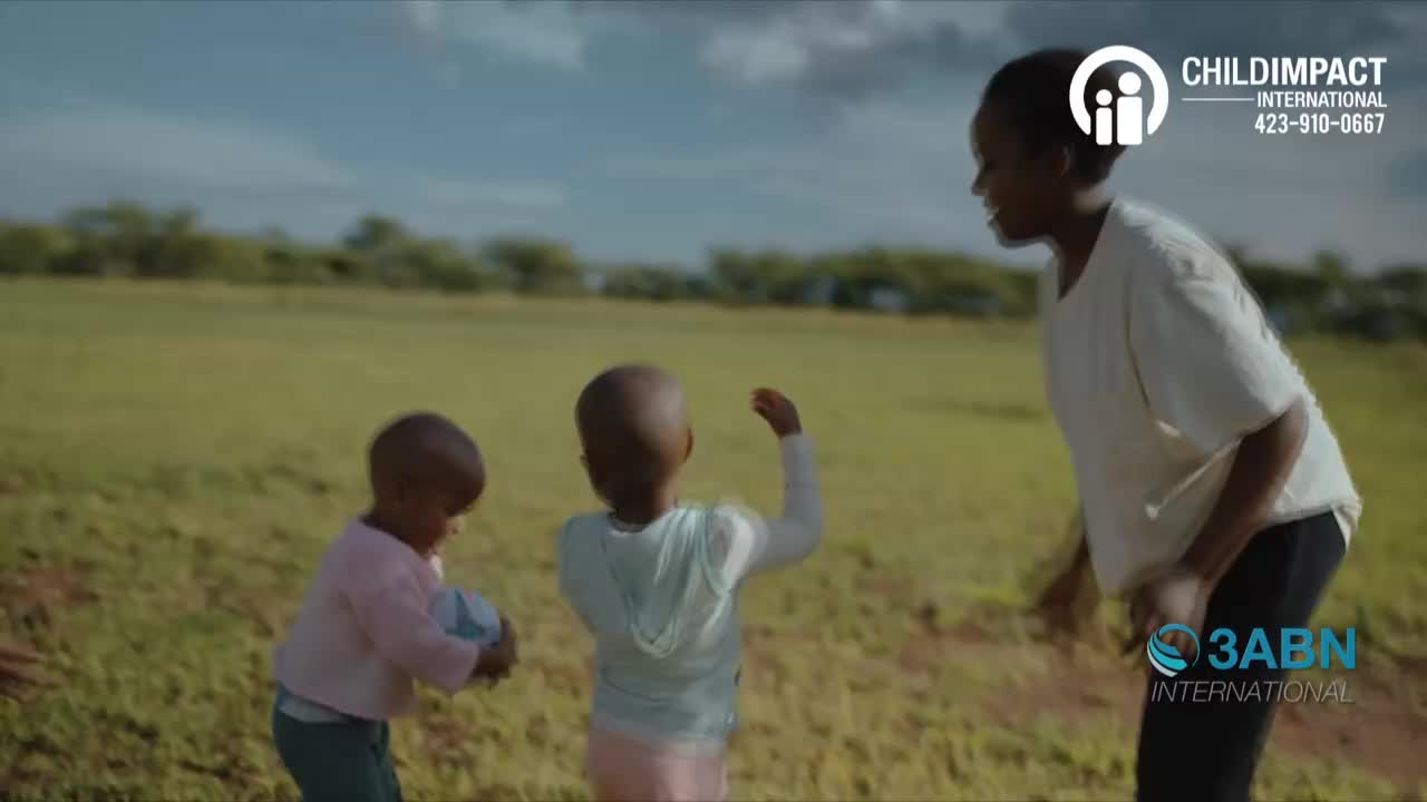 Two small children are playing with a ball in an open field while a woman smiles at them. The scene is bathed in sunlight, and the sky is a bright blue.
