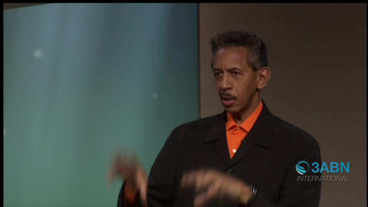 A man in a black suit and orange shirt gestures with both hands as he speaks. The 3ABN International logo is visible in the bottom right corner.
