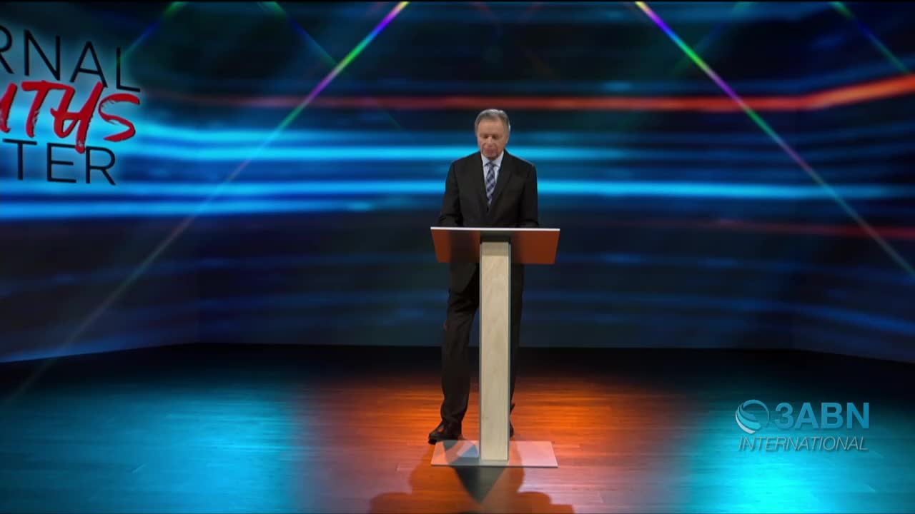 A man in a suit stands at a podium, speaking in front of a blue and orange backdrop. The 3ABN International logo is visible in the lower right corner.
