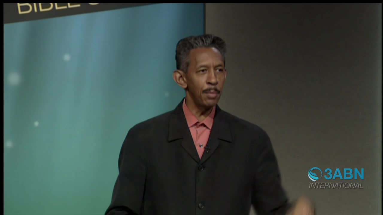 A man in a black jacket and pink shirt gestures while speaking, his gaze directed off-camera. The 3ABN International logo is visible in the bottom right corner.
