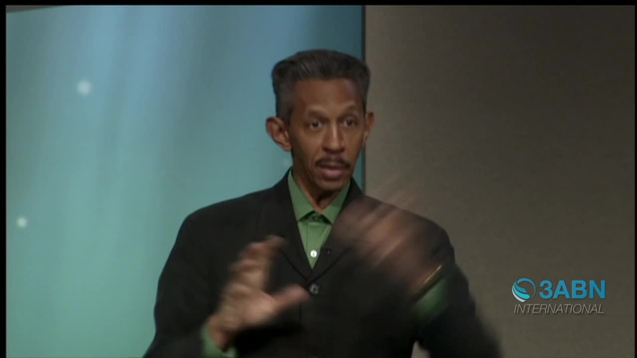 A man in a suit gestures with his hands, speaking into the camera for 3ABN International. His hands move quickly, and he seems to be emphasizing a point.
