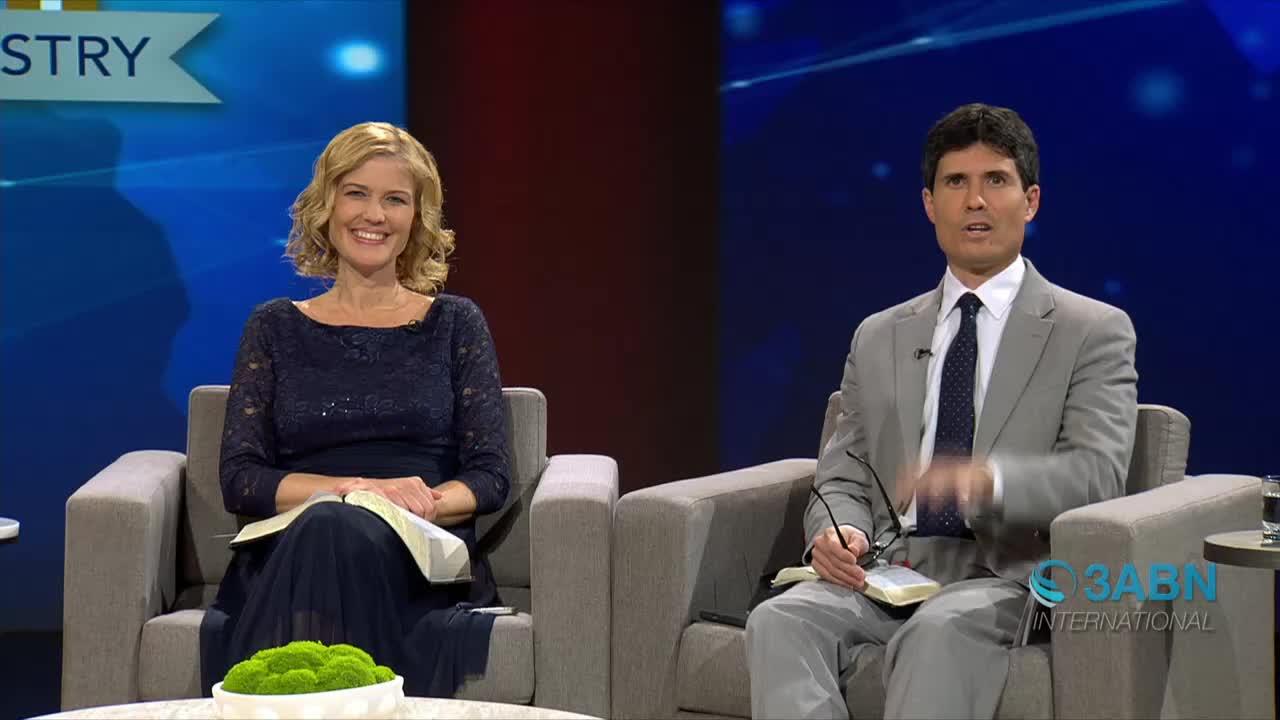 Two people are seated in armchairs, each holding a book, with the woman smiling at the camera. The man gestures with his hand as if he's speaking, and the 3ABN International logo is visible in the corner.
