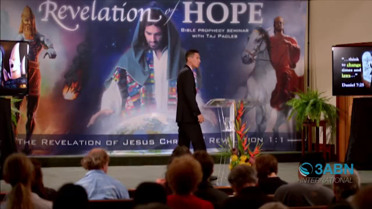 A man in a dark suit walks across the stage, past a backdrop advertising a Bible prophecy seminar. The 3ABN International logo is visible in the lower right corner.
