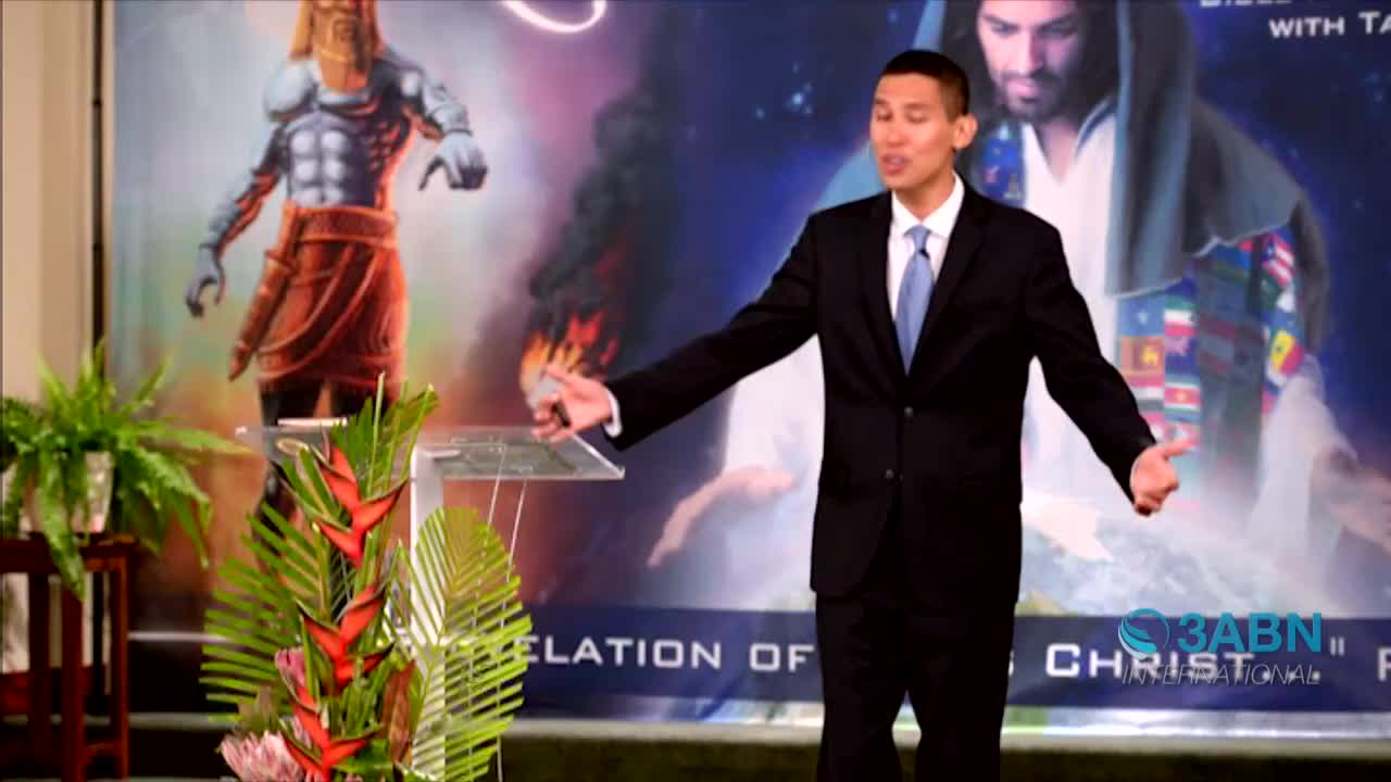 A man in a suit gestures expansively, speaking from behind a clear podium. Behind him, a backdrop depicts a painted figure and the logo for 3ABN International.
