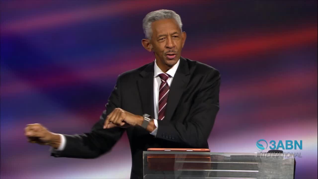 The man in the suit gestures with his right hand, pointing down, while his left fist is clenched. Behind him, the 3ABN International logo is visible on the right.
