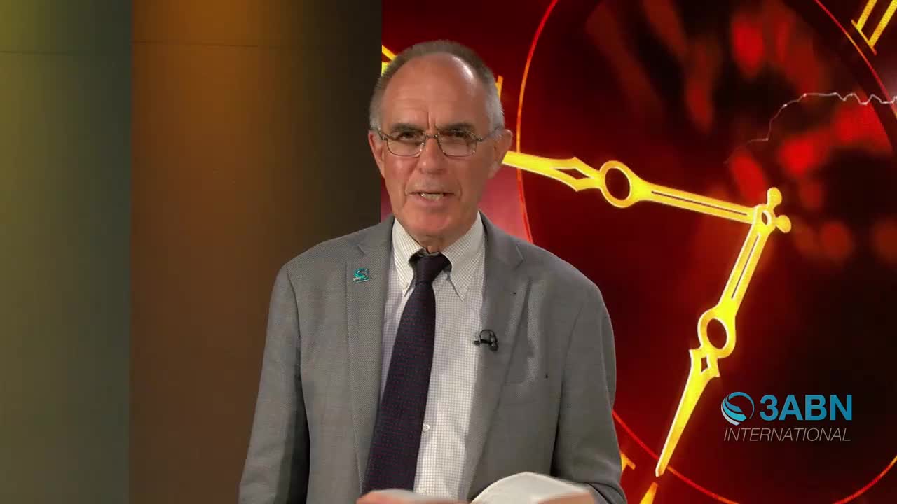 A man in a suit stands before a large clock face with glowing hands. He's holding a book open, ready to speak.