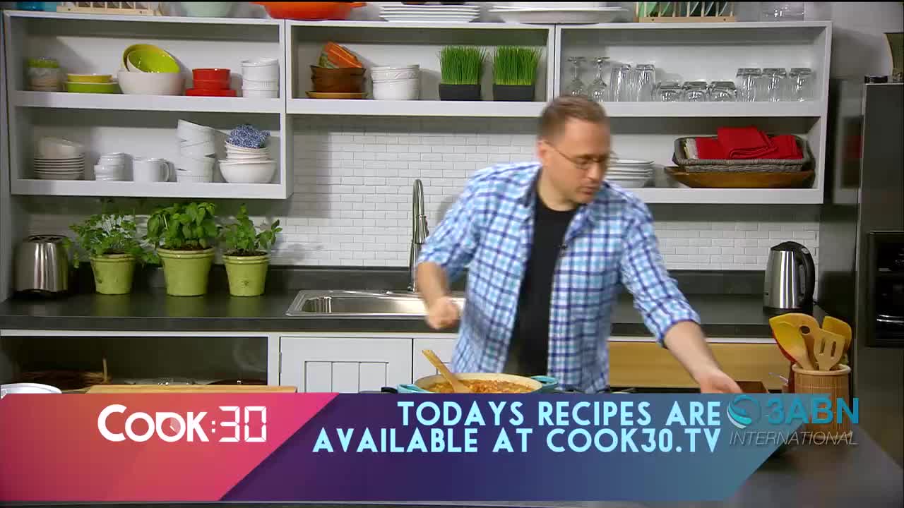 A man in a blue plaid shirt moves his hand over a pan of food on the counter. The "Cook:30" logo and "TODAYS RECIPES ARE AVAILABLE AT COOK30.TV" text appear on screen.