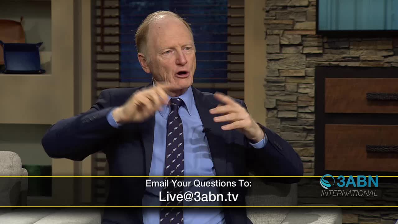 A man in a suit gestures with both hands while speaking. He's on a set for 3ABN International, a broadcast reaching across the United States.