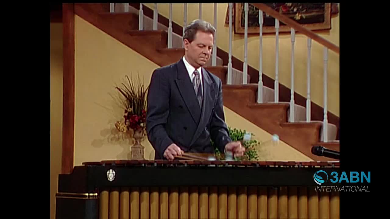 A man in a suit plays a marimba, his mallets striking the wooden bars. The 3ABN International logo appears in the corner of the screen, indicating this broadcast originates from the United States.