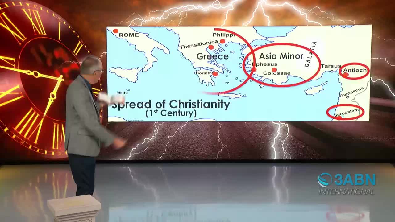 A man in a gray suit gestures toward a map showing the spread of Christianity across the Mediterranean. Lightning flashes behind him, illuminating a large clock face to his left.