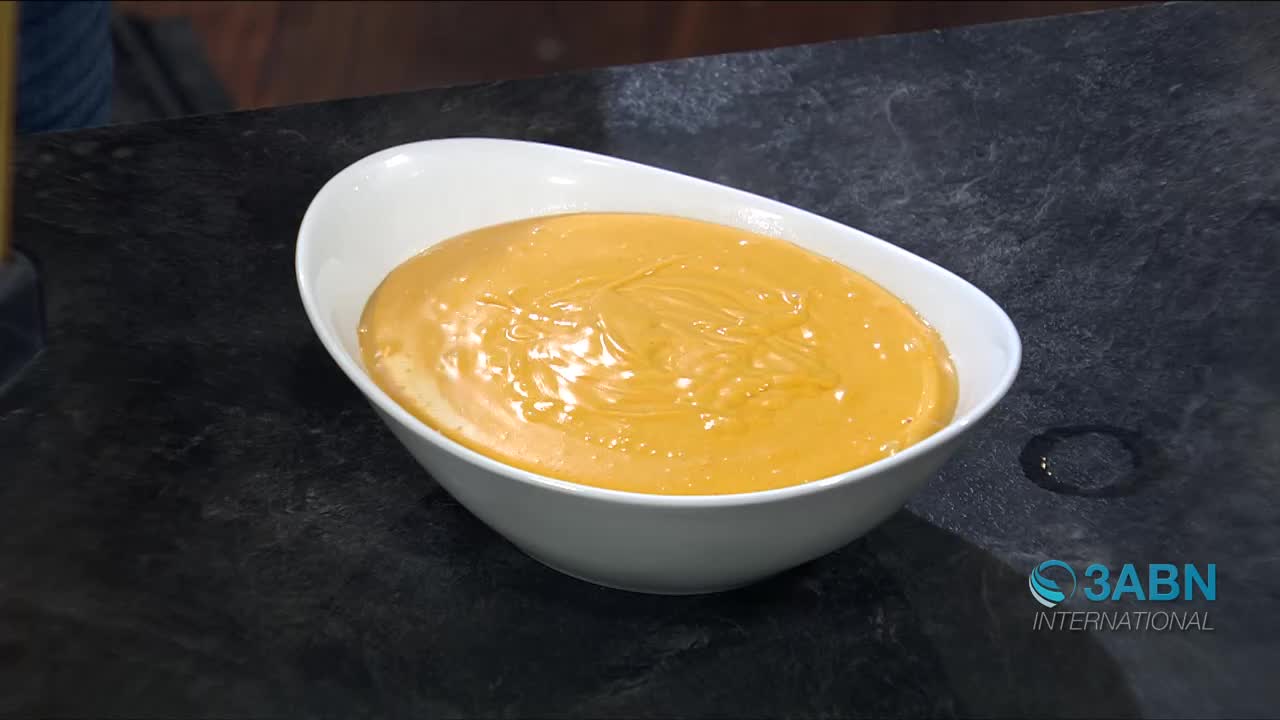 A bright orange sauce fills a white bowl on a dark counter. A small puddle of liquid sits to the right of the bowl.