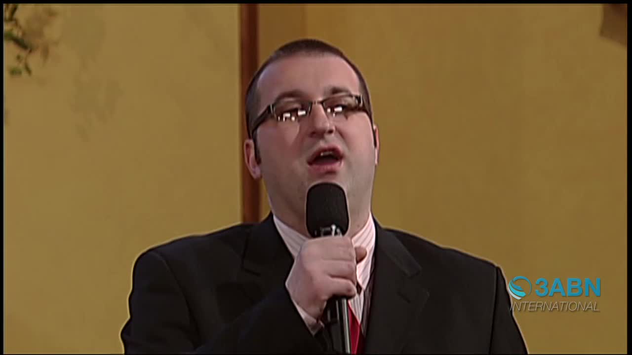 A man in a suit and tie sings into a microphone, his mouth open. The 3ABN International logo appears in the lower right corner.