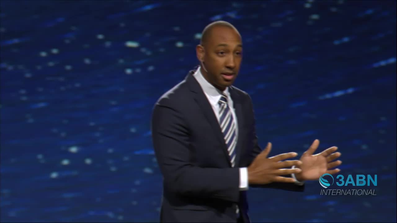 A man in a dark suit and striped tie gestures with both hands while speaking. The 3ABN International logo appears in the lower right corner of the screen.