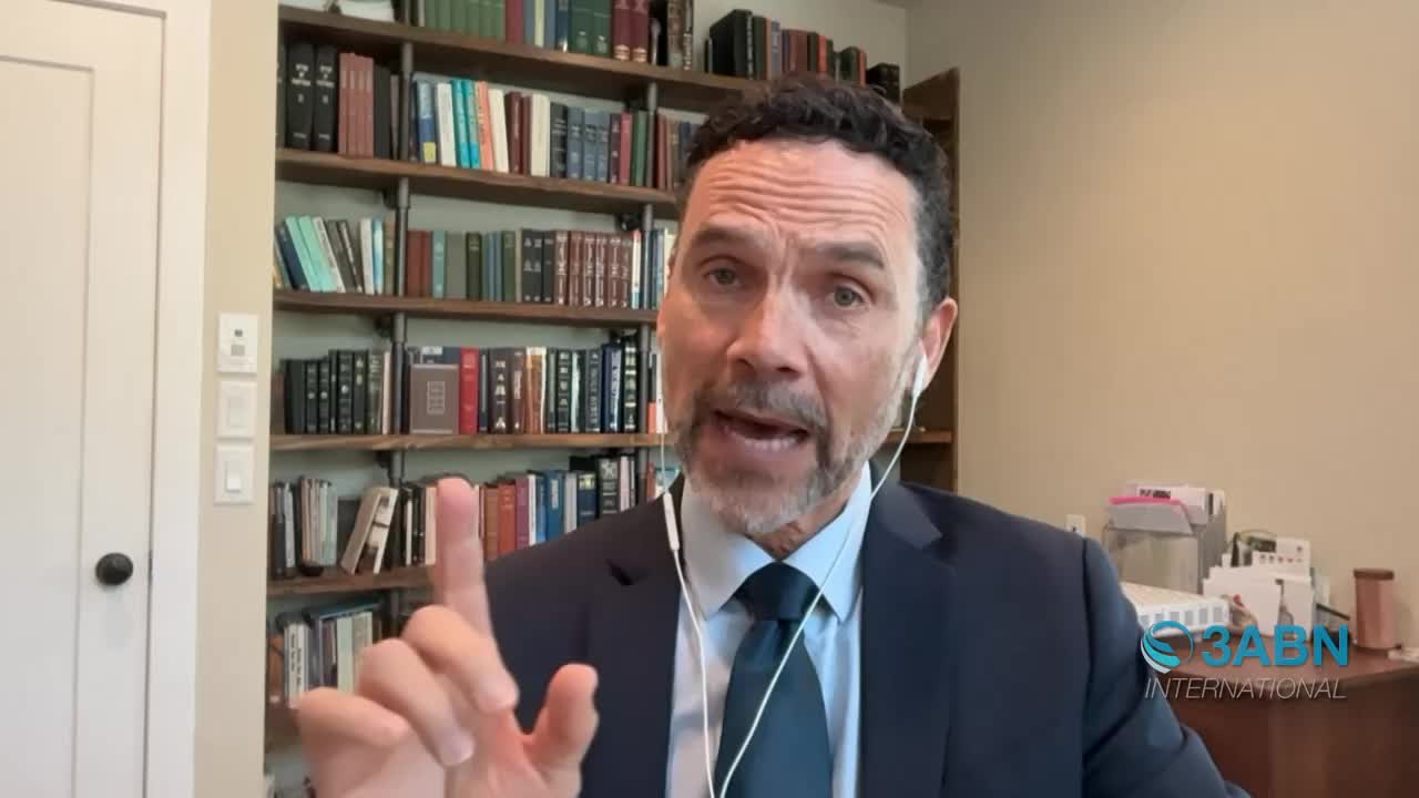 A man in a suit speaks directly to the camera, his right index finger raised as if making a point. Behind him, shelves overflow with books, and a small 3ABN International logo appears in the lower right corner.