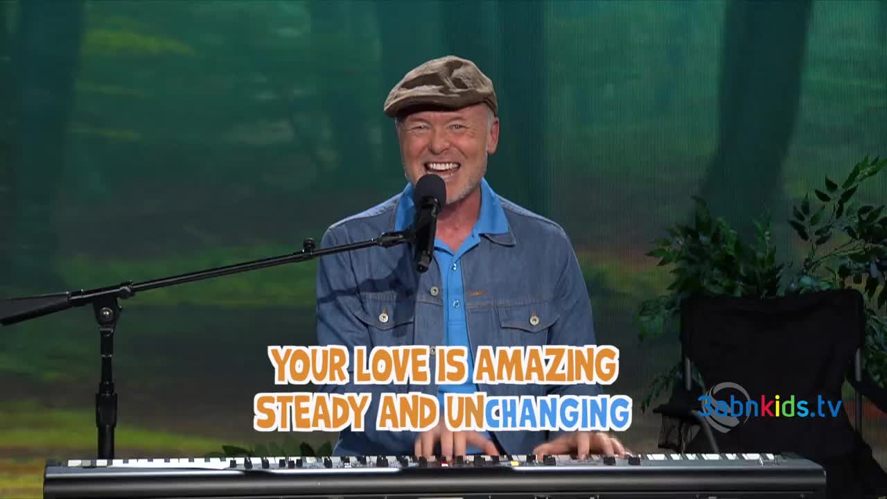 The man at the piano is singing, his hands dancing across the keys.  A caption on the screen reads "Your Love is Amazing."
