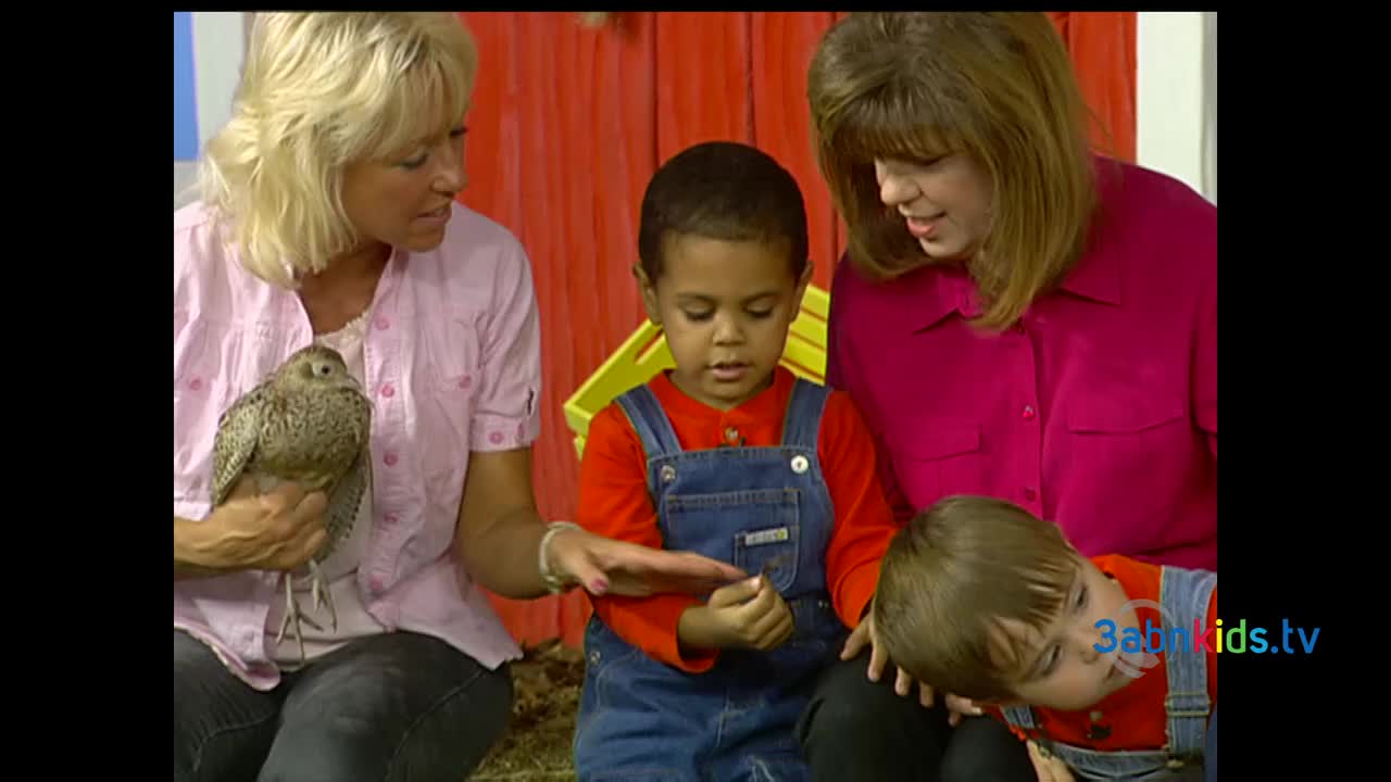 A woman with blonde hair holds a bird with speckled feathers, while a young boy in overalls looks at something in his hand. The scene appears to be from a 3ABN Kids show, filmed in the United States.
