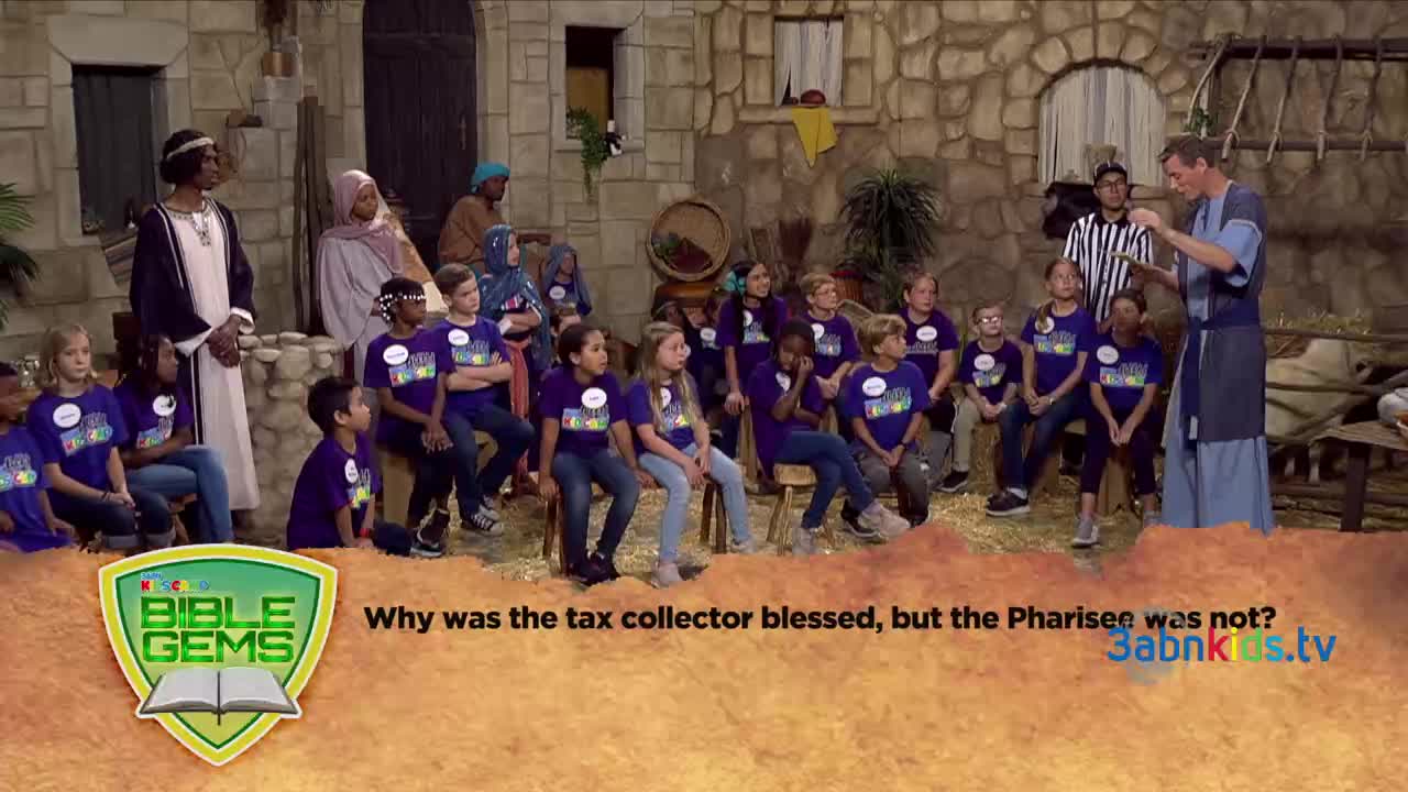 A man in a blue robe gestures as he speaks to a group of children wearing purple t-shirts. Behind them, people dressed in period costumes sit on a stage set for a 3ABN Kids production.
