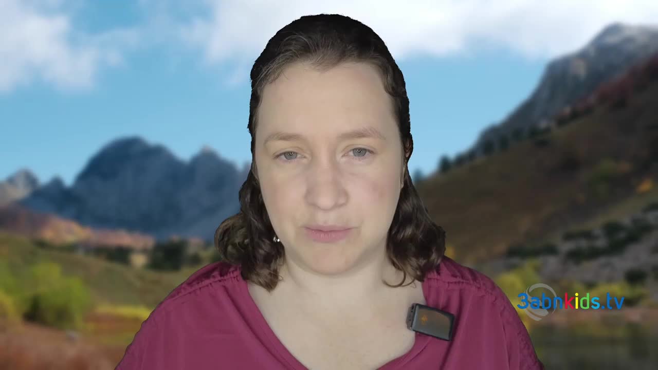 A woman in a maroon shirt is speaking directly at the camera. Behind her, a backdrop shows a mountain range under a blue sky.
